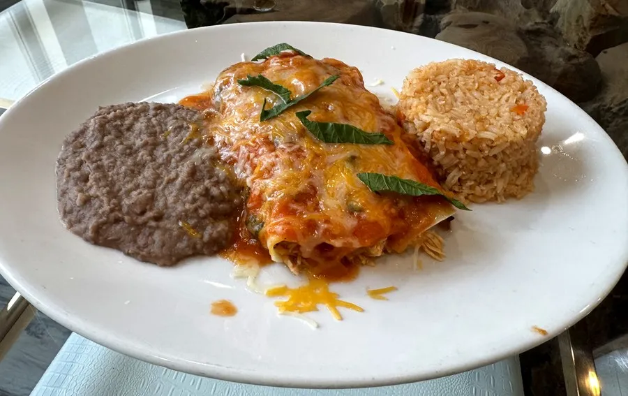 Enchiladas topped with melted cheese, with Mexican rice and refried beans