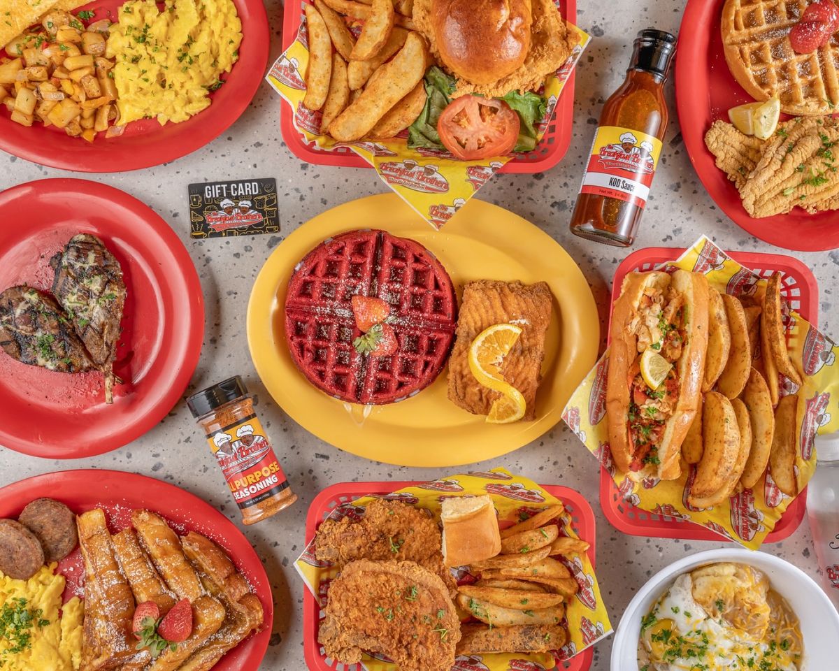 A full table of Breakfast Brothers plates: waffles, wings, lamb chops, catfish, and sides on red and yellow plates