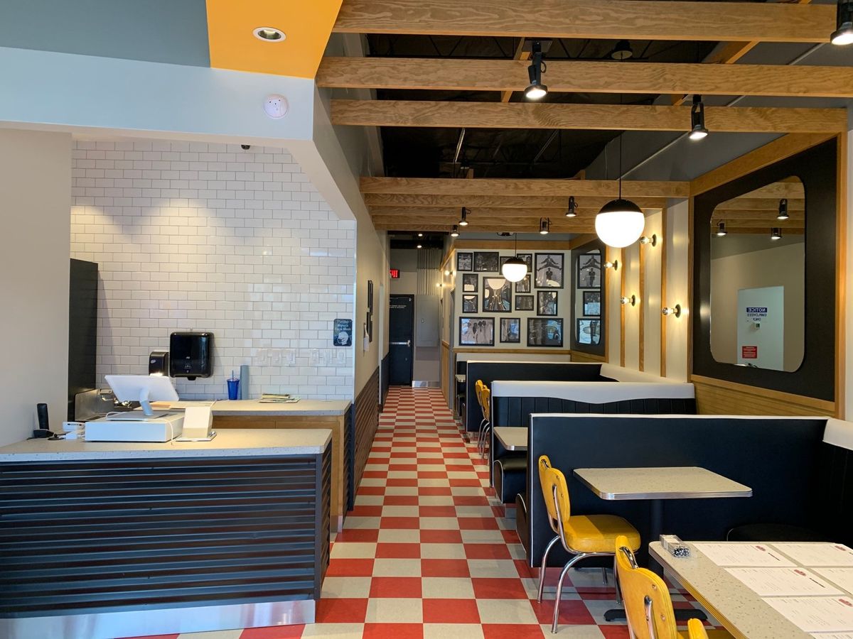 Inside the Breakfast Brothers dining room: red and white checkerboard floor, navy booths, yellow chairs, wood beam ceiling